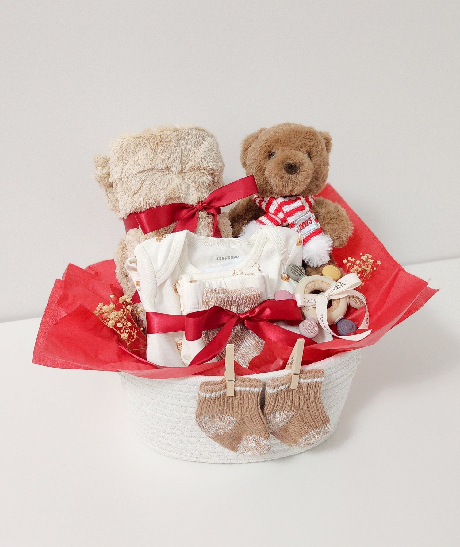 Two teddy bears in a decorative basket with red ribbons on a white background

